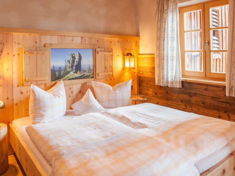 Das gemütliche Schlafzimmer aus Holz im Kampenwand Doppelzimmer mit großem Doppelbett und einladender Beleuchtung.