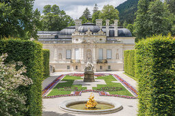 Eindrucksvolles Schloss mit Garten, Statue und goldenem Springbrunnen.
