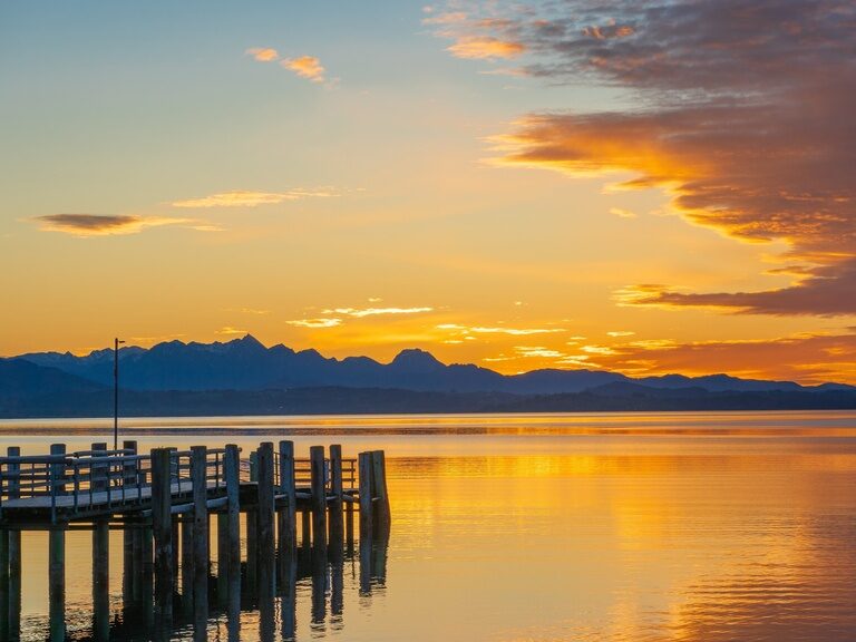 Ein malerischer Sonnenuntergang über der Wasseroberfläche des Chiemsees, es ist zudem ein Steg zu sehen.