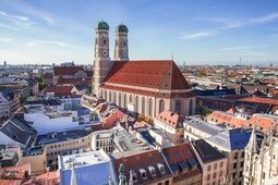 Sonniger Tag vor einer imposanten Kirche in München, umgeben von zahlreichen Stadthäusern
