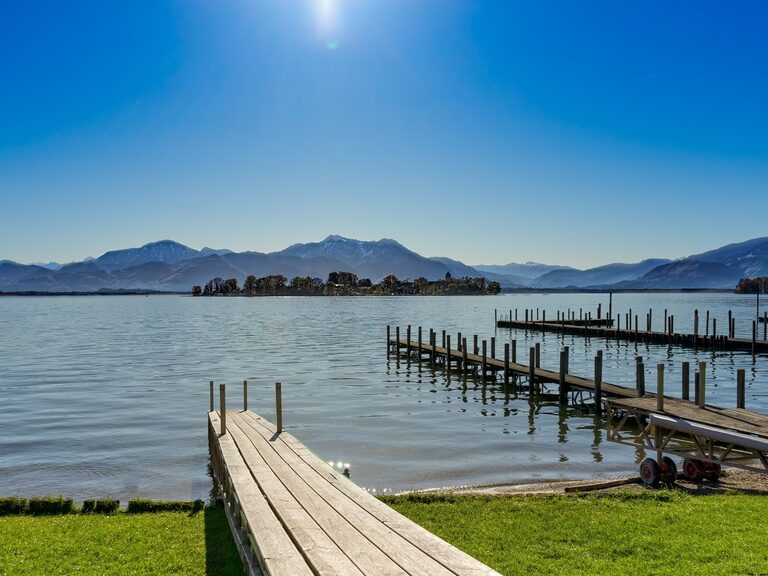 Holzsteg am Chiemsee, dahinter sonnige Alpenlandschaft