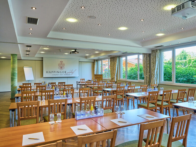 Ein Tagungsraum mit aufgestellten Tischen, einer Leinwand, stilvoller Beleuchtung und Getränken