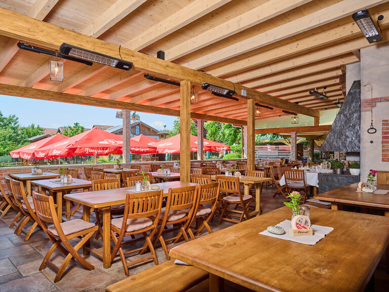 Terasse im Sommer im 3-Sterne-S-Hotel und Landgasthof Happinger Hof beim Chiemsee Überdachte Terasse mit Holzstühlen- und Tischen an sonnigem Tag