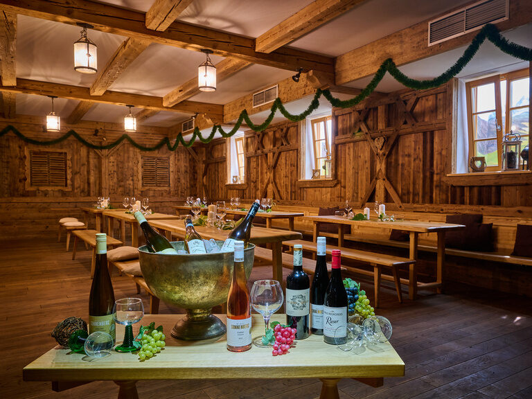 Tisch mit Weinflaschen im 3-Sterne-S-Hotel und Landgasthof Happinger Hof beim Chiemsee Tisch in traditioneller Weinstube: Weinflaschen, Gläser, Schinken, Käse, Weintrauben, Kühlerbehälter