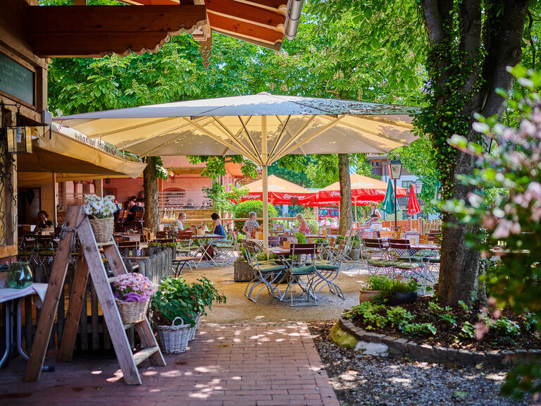 Traditioneller Biergarten mit Holzklappstühlen und -tischen, Sonnenschirmen, Blumen