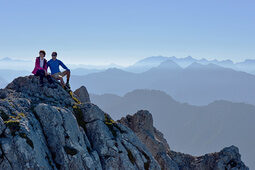 Zwei Wanderer genießen Ausblick auf Steinen auf Gipfel im Alpengebirge