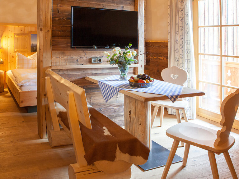 Das helle Wohnzimmer des Kampenwand Doppelzimmers mit Stühlen und Tisch aus Holz sowie TV an der Wand.